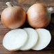 Two whole ovation onions and a few sliced pieces of onion on a wooden surface.