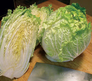 Two heads of  China Express Napa cabbage on a wooden surface with a knife in the foreground.