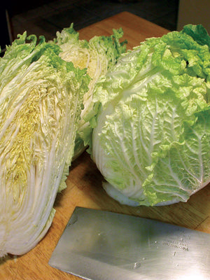Two heads of  China Express Napa cabbage on a wooden surface with a knife in the foreground.