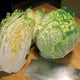 Two heads of  China Express Napa cabbage on a wooden surface with a knife in the foreground.
