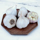 Five rosewood garlic bulbs on a wooden cutting board with a marble background
