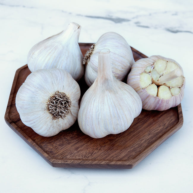 Five rosewood garlic bulbs on a wooden cutting board with a marble background