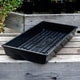 Black SUNPACK® MEGA Color I.D. plastic tray on a wooden surface with plants in the background