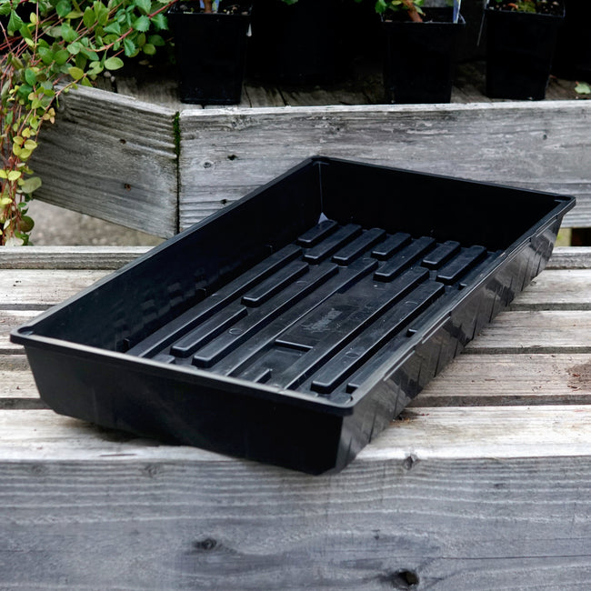 Black SUNPACK® MEGA Color I.D. plastic tray on a wooden surface with plants in the background