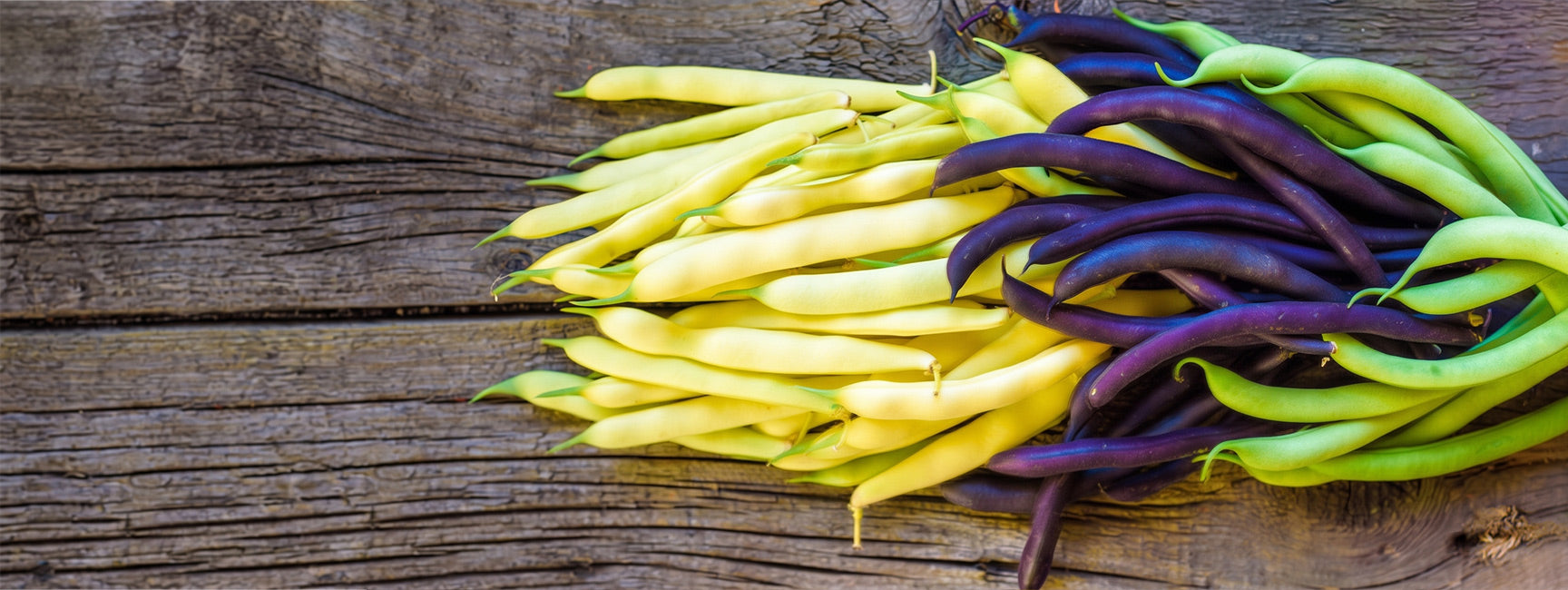 Yellow, green, and purple beans on a wooden surface
