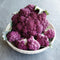 Close-up of DePurple cauliflower showcasing lilac-purple florets with green outer leaves on light background