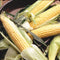 Close-up of Golden Jubilee sweet corn ears with partially husked deep yellow kernels on a dark bowl background