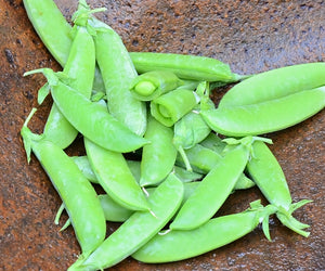 Top-down close-up of Super Sugar Snap pea pods showing plump, bright green, stringless pods in a rust-colored bowl