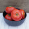 Close up of Oregon Spring tomatoes in a black bowl showcasing smooth, round red slicing fruit on a white wooden surface